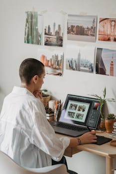 Focused woman editing photos on a laptop at a cozy home office with creative wall decor.